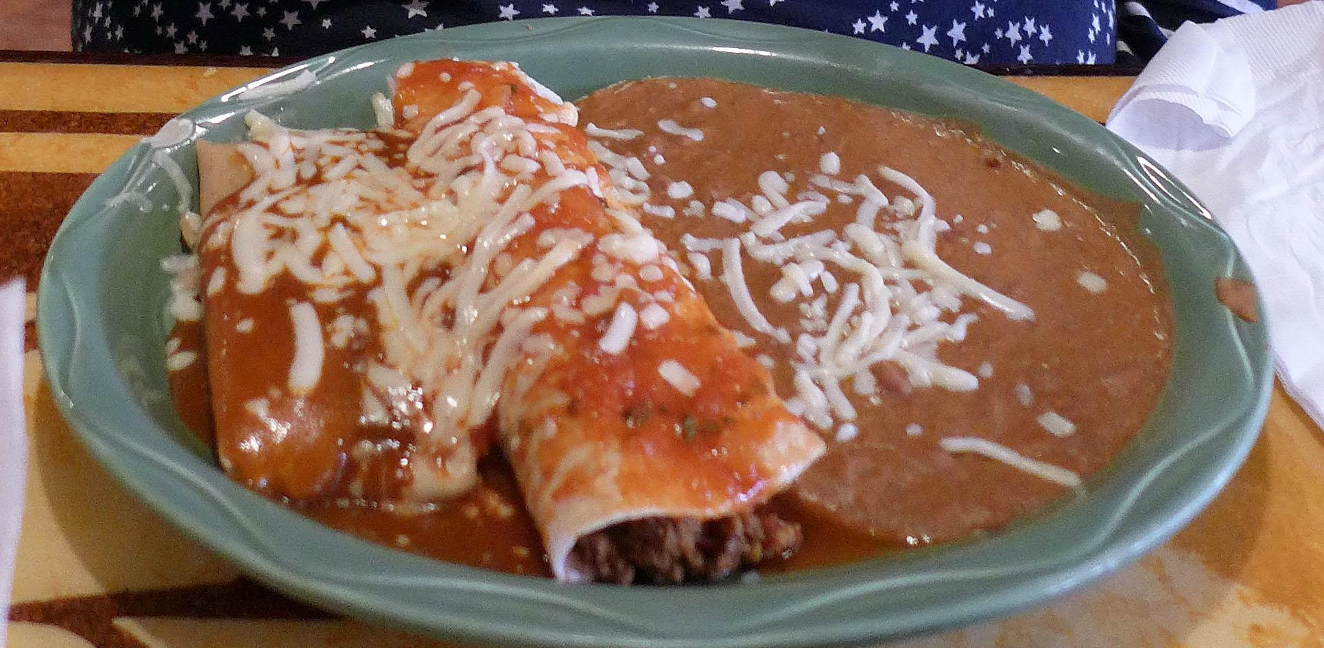 An enchilada smothered in red sauce and melted cheese, served with refried beans