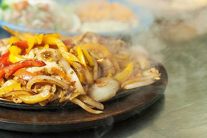 A sizzling fajitas skillet with grilled chicken, peppers and onions, steam rising off the cast iron