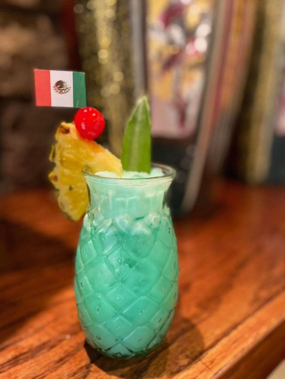 Blue tiki cocktail with pineapple, cherry and a Mexican flag